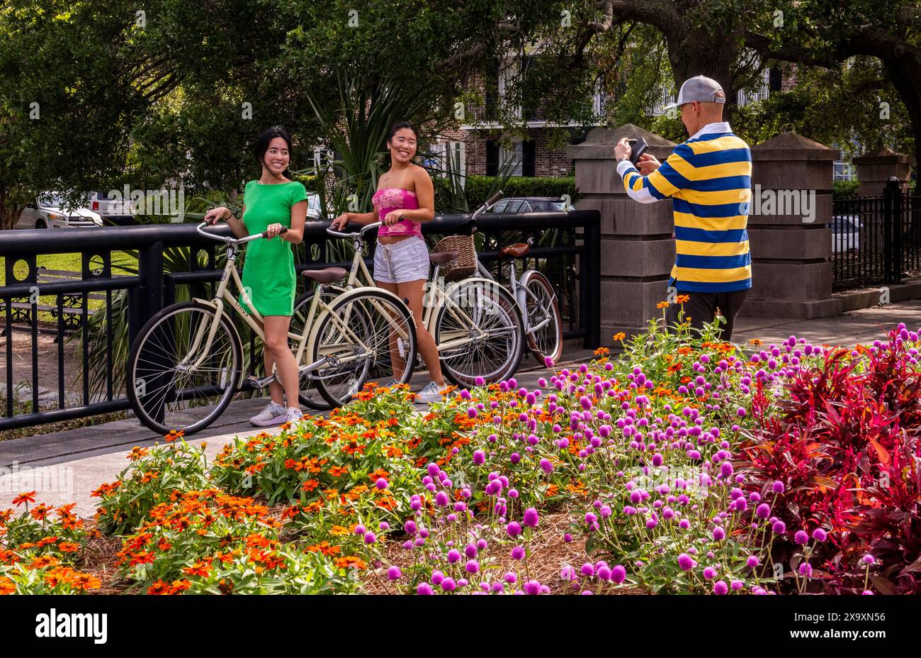 Un uomo che indossa un top dai colori vivaci scatta una foto di due giovani donne che sorridono e indossano abiti molto luminosi. Foto Stock