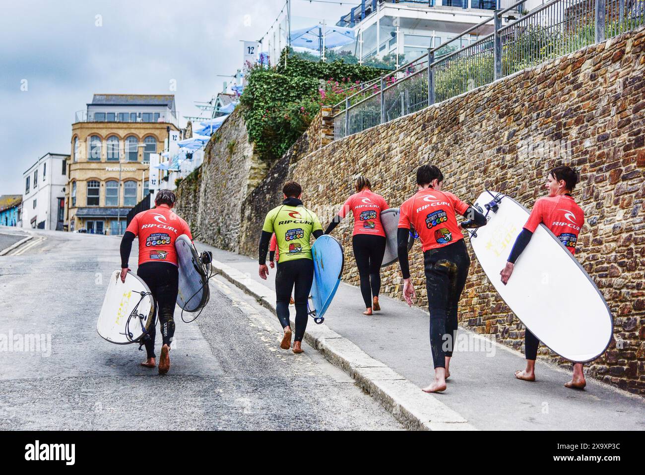Un istruttore di surf e un gruppo di studenti che portano le loro tavole da surf dopo una lezione di surf nel centro di Newquay nel Regno Unito. Foto Stock
