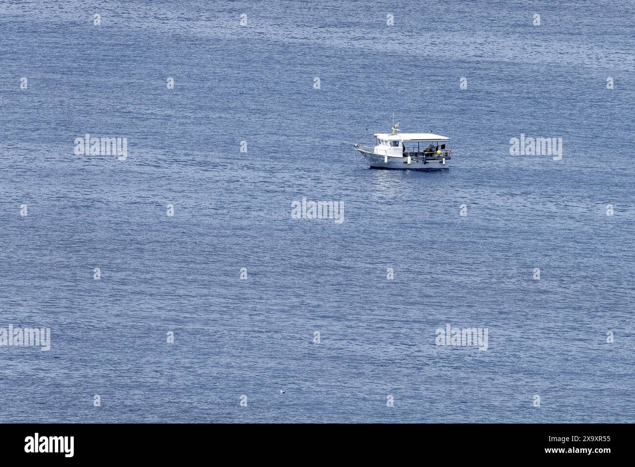 Una barca da pesca solitaria galleggia sulle calme acque blu di Minorca. La vasta distesa del mare enfatizza la natura serena e tranquilla della scena. Foto Stock