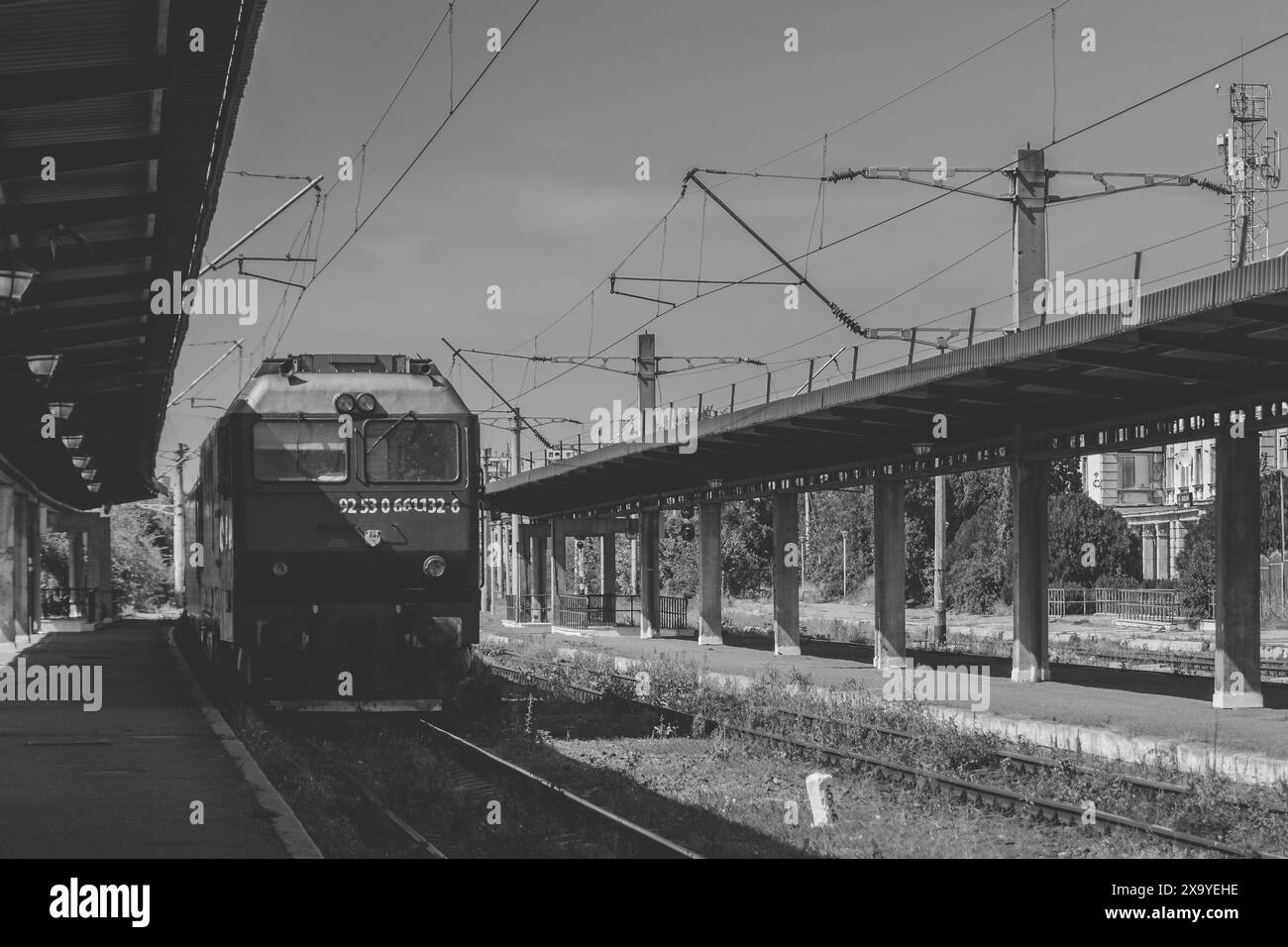 Un treno percorre i binari di una stazione sopraelevata con erba ed erbacce a Iasi, Romania Foto Stock