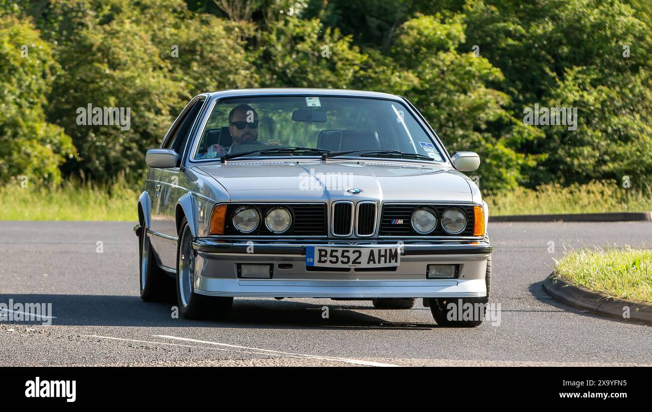 Stony Stratford, Regno Unito - 2 giugno 2024: BMW M635 csi serie 6 argento 1985 che guida su una strada di campagna britannica Foto Stock