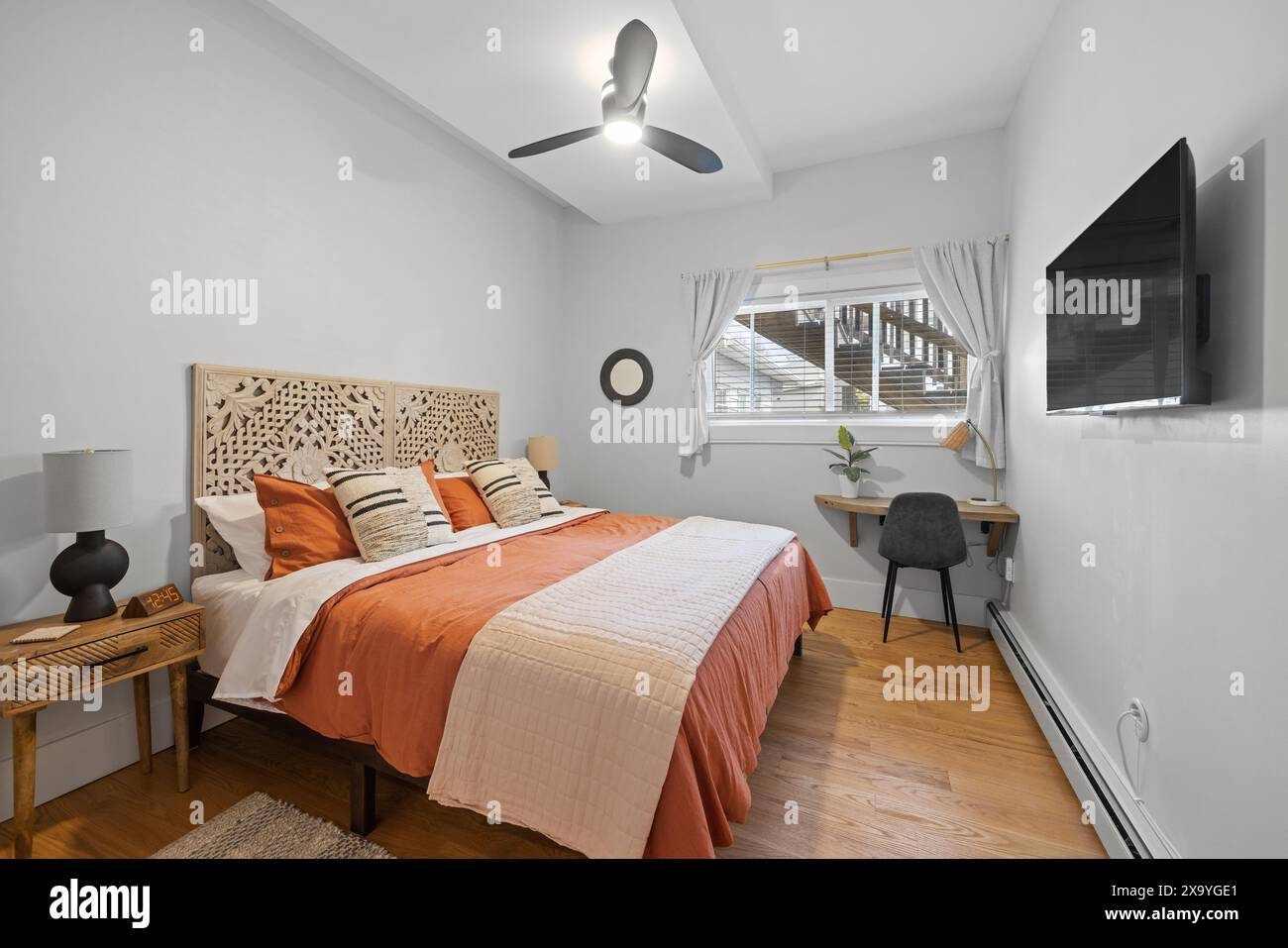 Un'accogliente camera da letto con TV, finestre e pavimenti in parquet Foto Stock