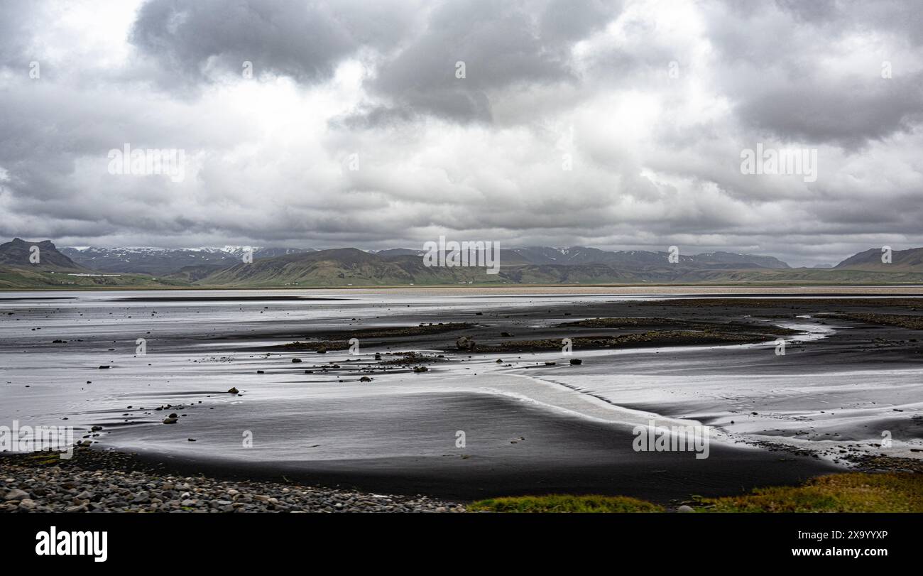 Vik, sabbia nera islandese contro il mare blu profondo, crea una scena accattivante. Il paesaggio vulcanico aggiunge un tocco drammatico Foto Stock