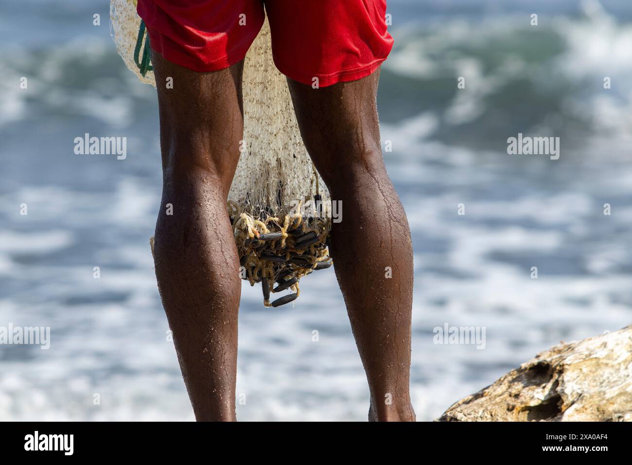 Un uomo che tira dentro una rete da pesca con una cattura di successo Foto Stock
