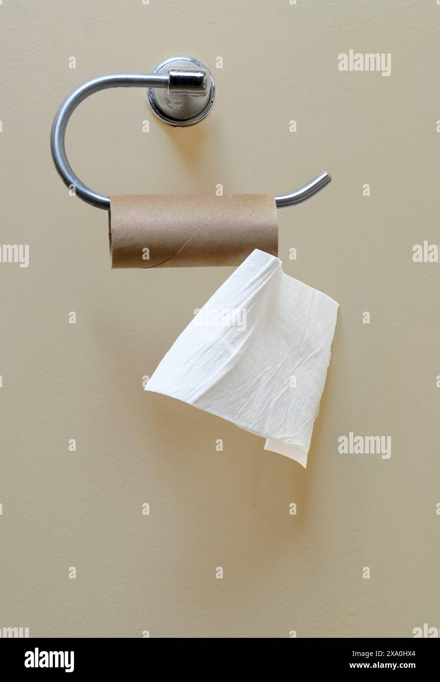 Colpo verticale di un rotolo di carta igienica quasi vuoto appeso al porta carta igienica sulla parete del bagno. Foto Stock