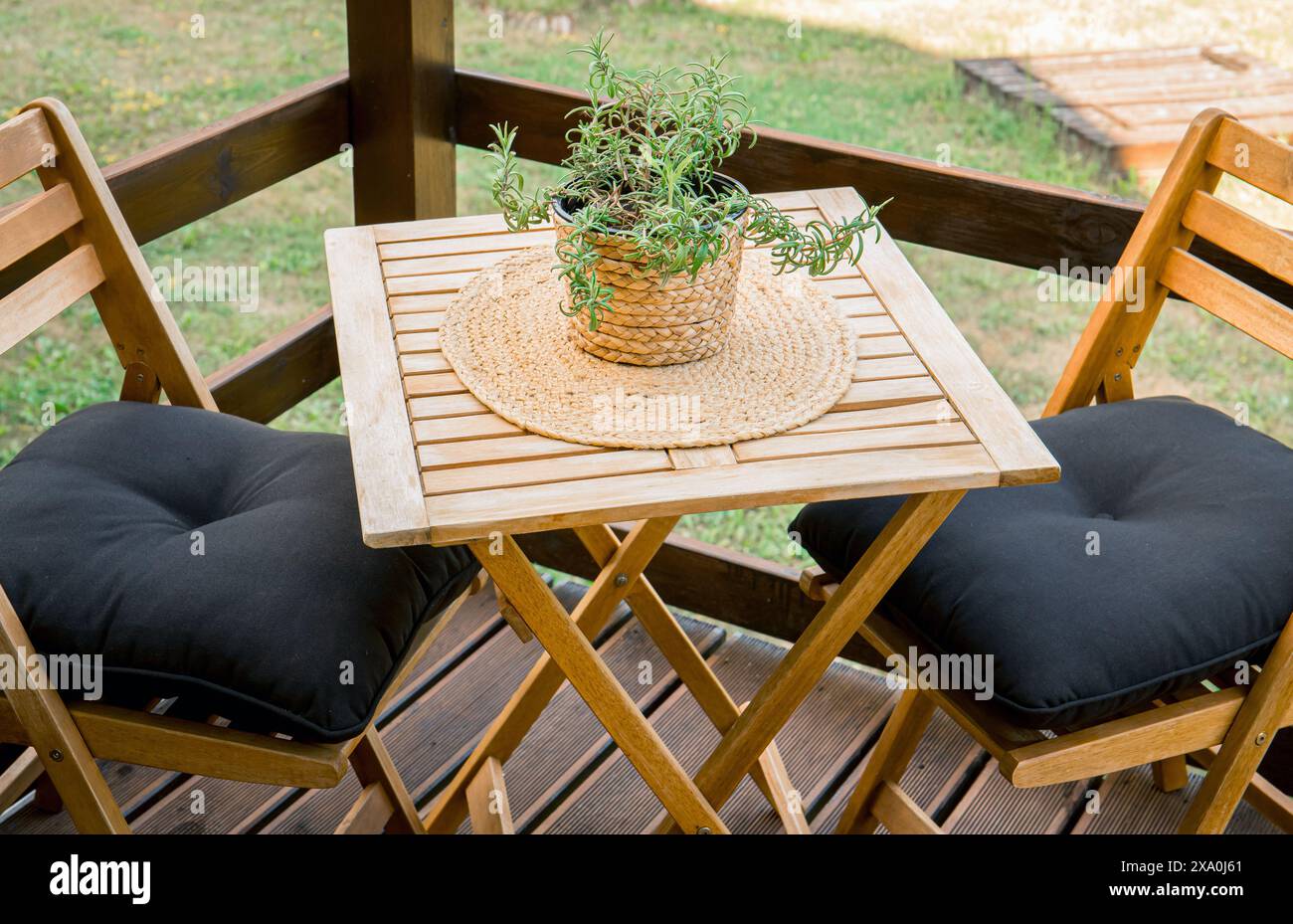 Vista ravvicinata dei mobili da giardino in legno collocati su un piccolo balcone. Vaso rosmarino sul tavolo, tappetino naturale. Foto Stock