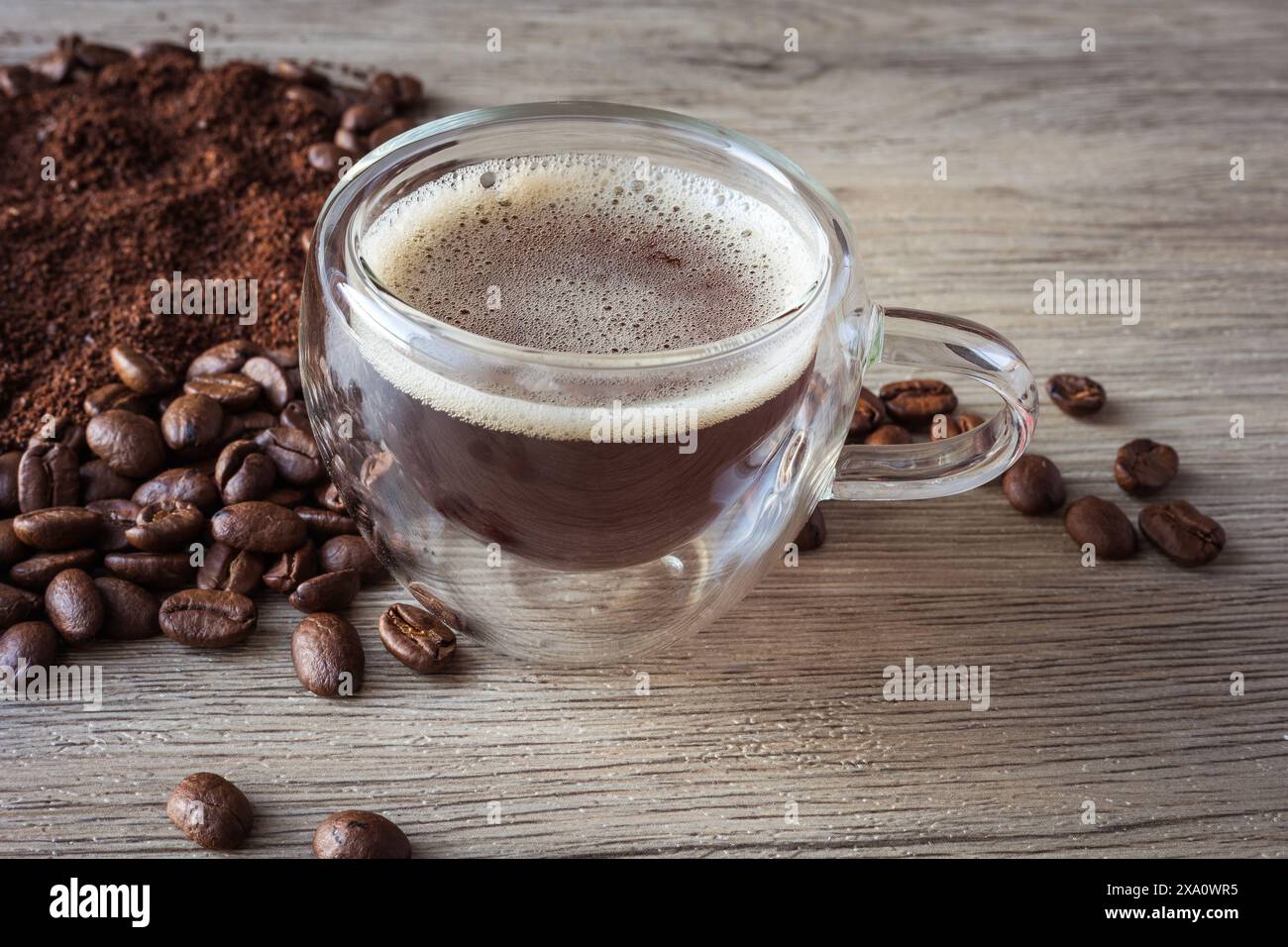 tazze di vetro con caffè americano circondate da chicchi di caffè e caffè macinato su una tavola di legno Foto Stock