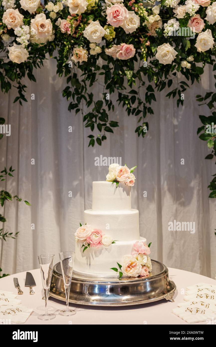 Una foto verticale di una torta nuziale su un tavolo da un arco floreale Foto Stock