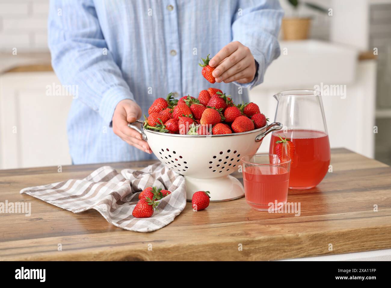 Donna con fragole fresche nel colino e succo di fragole su un tavolo di legno in cucina Foto Stock