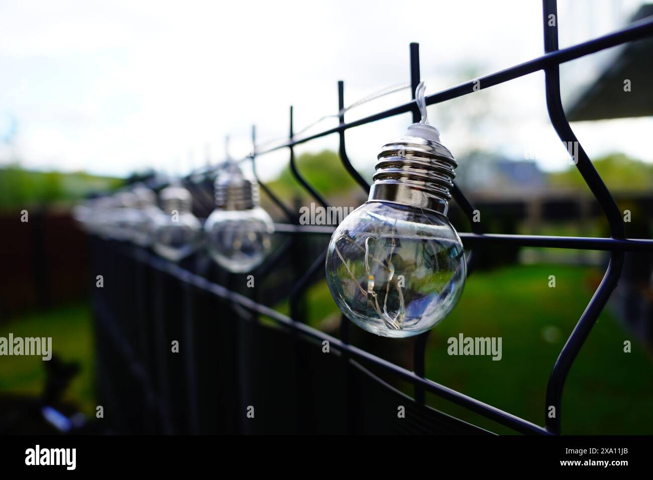 Le lampadine appese su una recinzione metallica vicino a un campo erboso Foto Stock