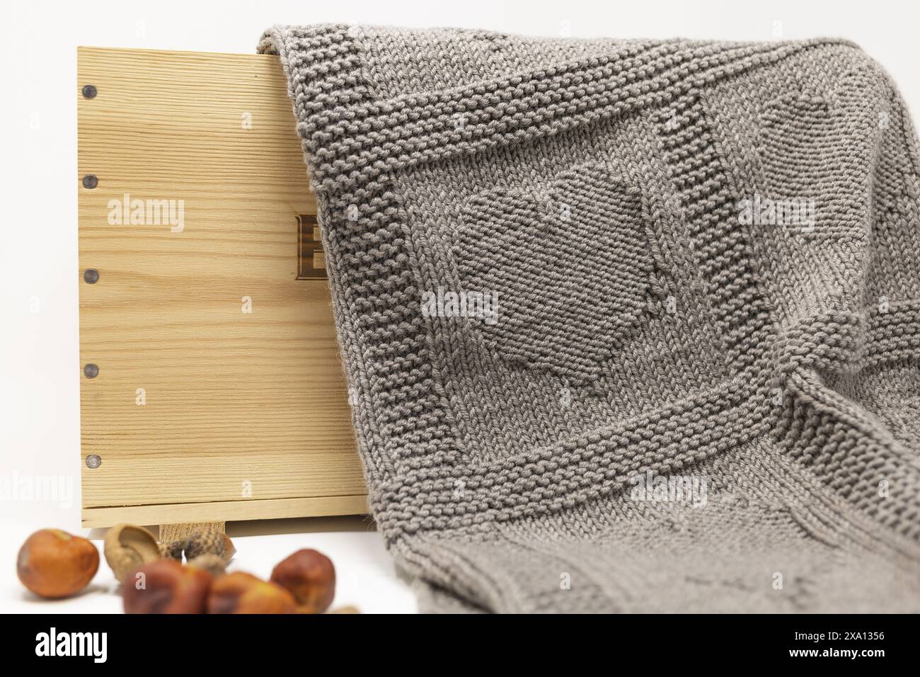 Foto ravvicinata di una coperta marrone in lana lavorata a mano con motivo Hearts in una scatola di legno su sfondo bianco Foto Stock