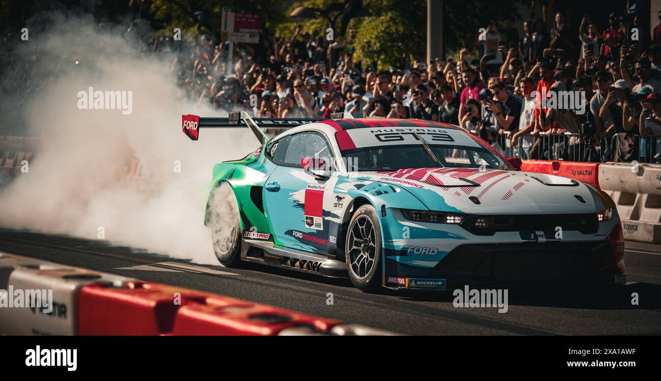 Un'auto si sposta lungo la strada della città e la folla si riunisce per assistere all'evento DC Red Bull Foto Stock