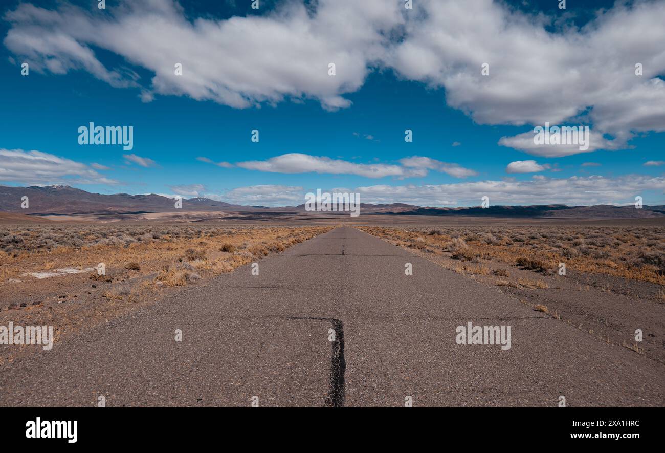 Un'autostrada deserta in un deserto arido con un cielo azzurro cristallino in Nevada Foto Stock