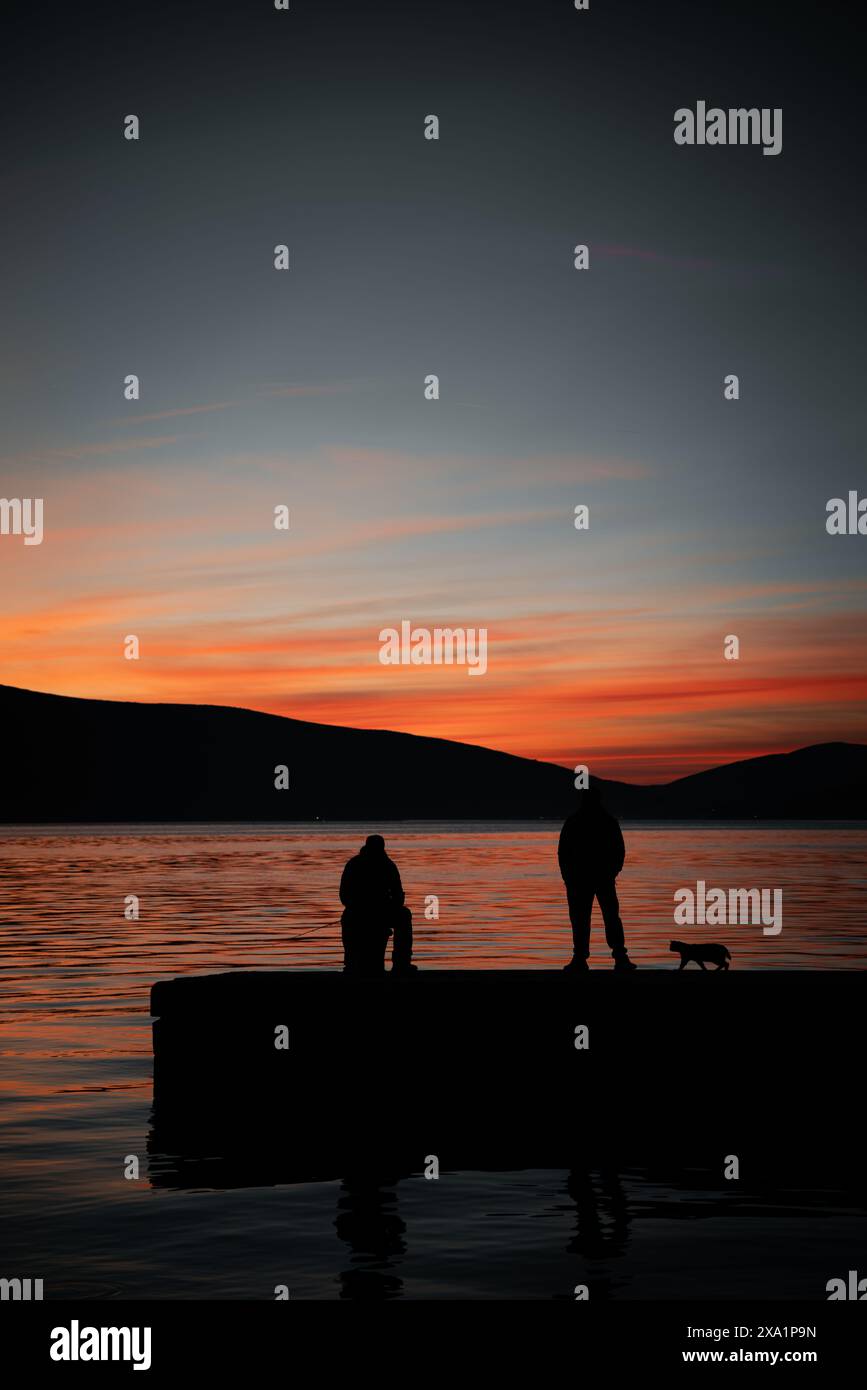 I due uomini con un gatto sul molo al tramonto Foto Stock