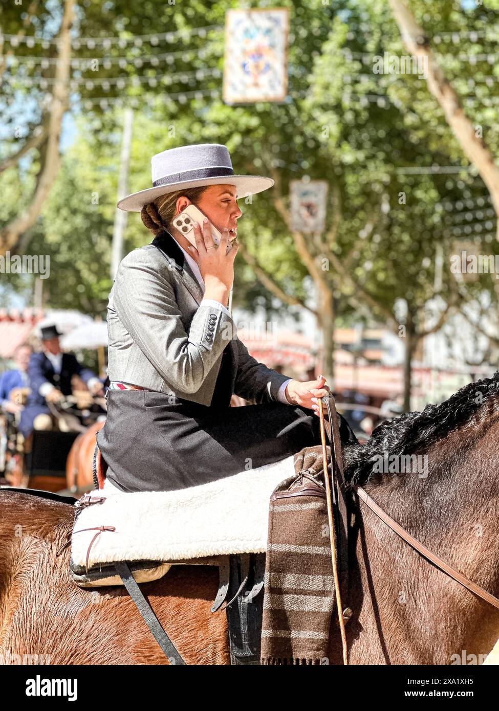 Una donna a cavallo chatta su smartphone durante Feira de Abril a Siviglia in Spagna Foto Stock