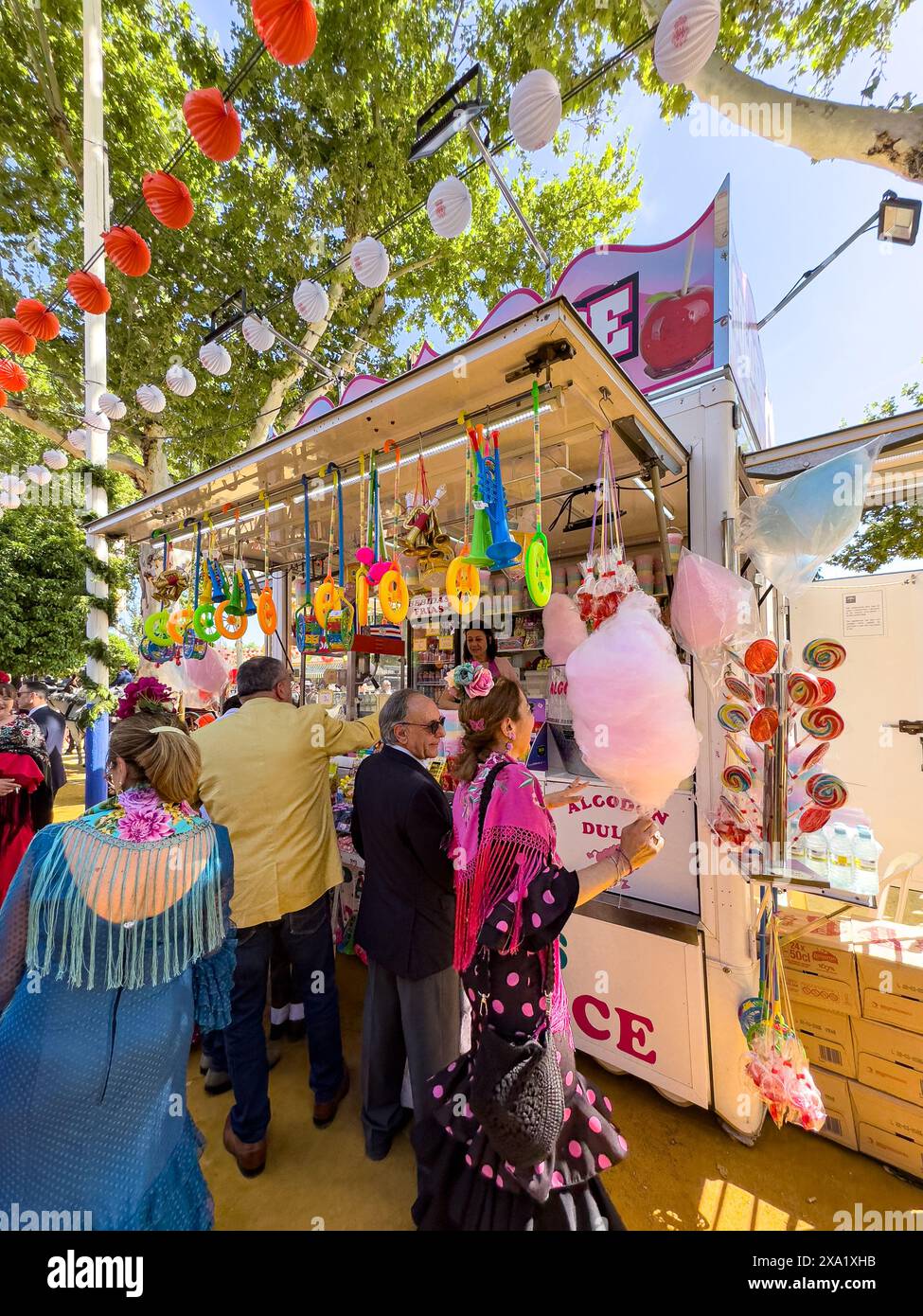 I visitatori del festival indossano abiti tradizionali al Feira de Abril di Siviglia, facendo la fila a un venditore di dolci durante il festival della durata di una settimana Foto Stock
