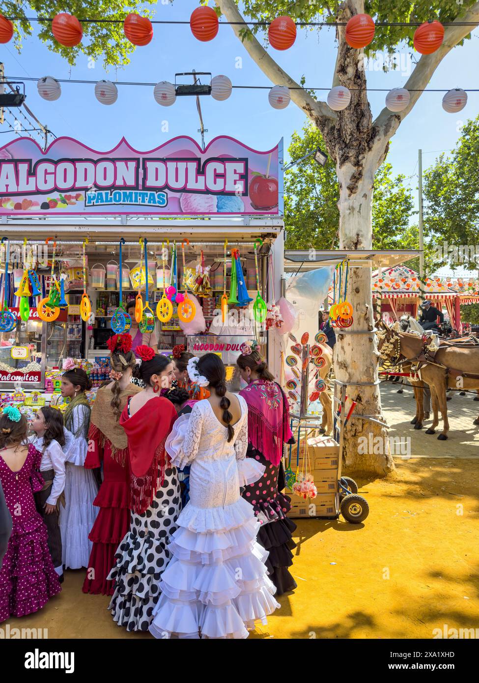 I visitatori del festival indossano abiti tradizionali al Feira de Abril di Siviglia, facendo la fila a un venditore di dolci durante il festival della durata di una settimana Foto Stock