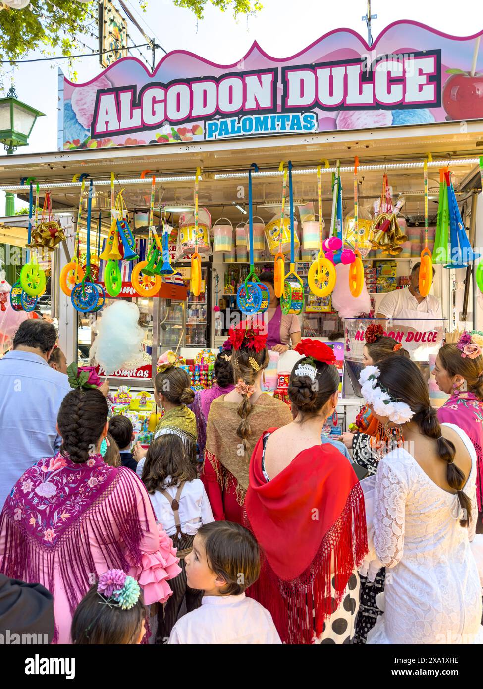 I visitatori del festival indossano abiti tradizionali al Feira de Abril di Siviglia, facendo la fila a un venditore di dolci durante il festival della durata di una settimana Foto Stock