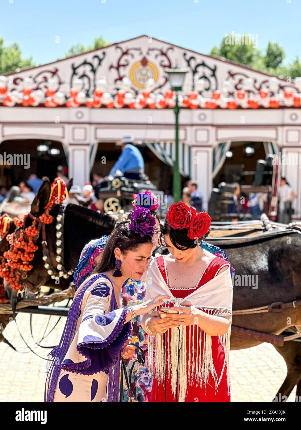 Due donne in abiti di flamenco vicino a una carrozza trainata da cavalli alla Feria de Abril, nota anche come la Fiera di Siviglia Foto Stock