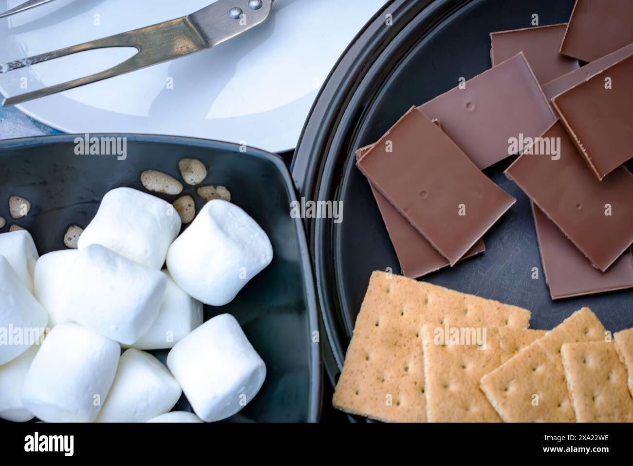 Ingredienti per fare gli smores... Vista dall'alto con cioccolato, cracker graham, marshmallow e forchette per arrostire i marshmallow. Foto Stock