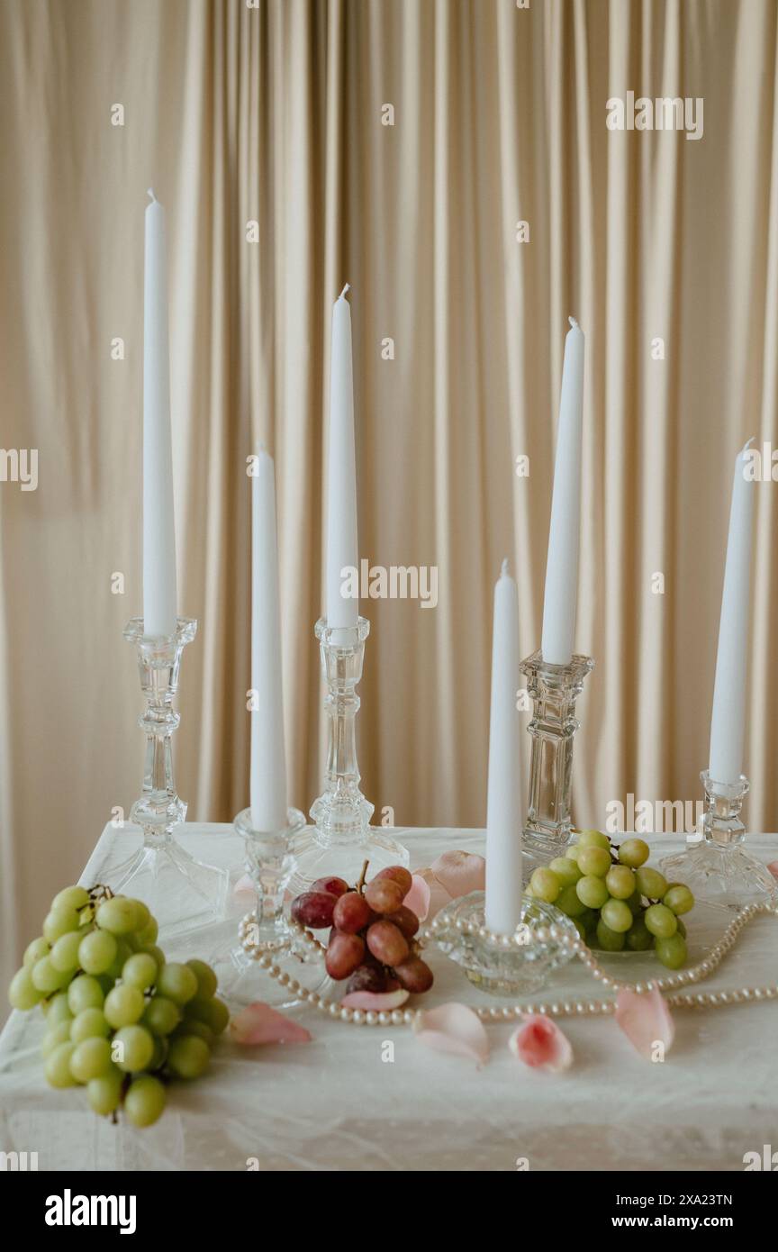 Un candelabro e un nero di bianco acceso con uva, perle e petali di rosa rosa. Foto Stock