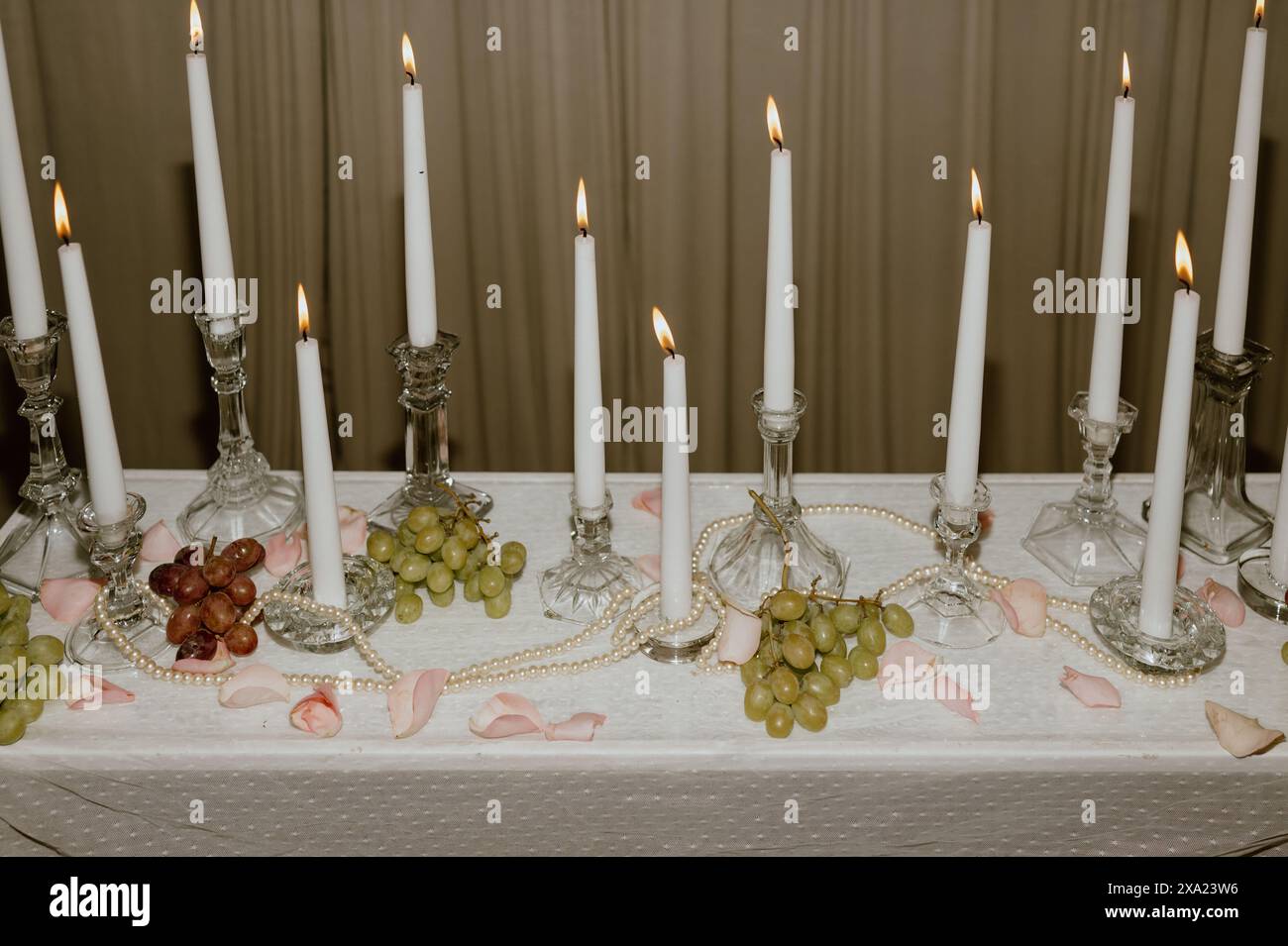 Un candelabro e un nero di bianco acceso con uva, perle e petali di rosa rosa. Foto Stock