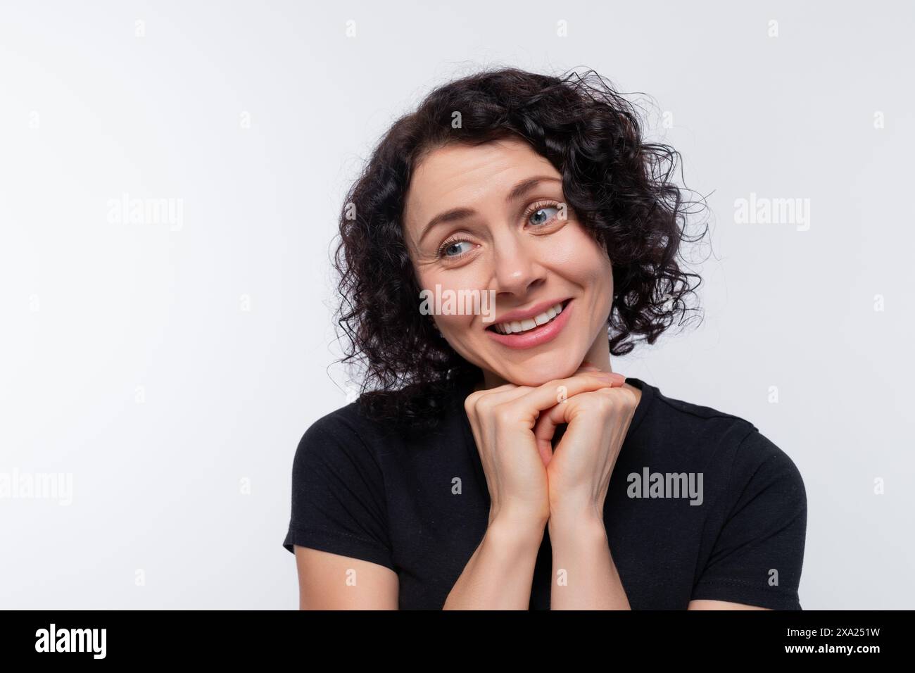 Una modesta bruna con capelli ricci indossa una maglietta nera su uno sfondo con spazio di copia Foto Stock