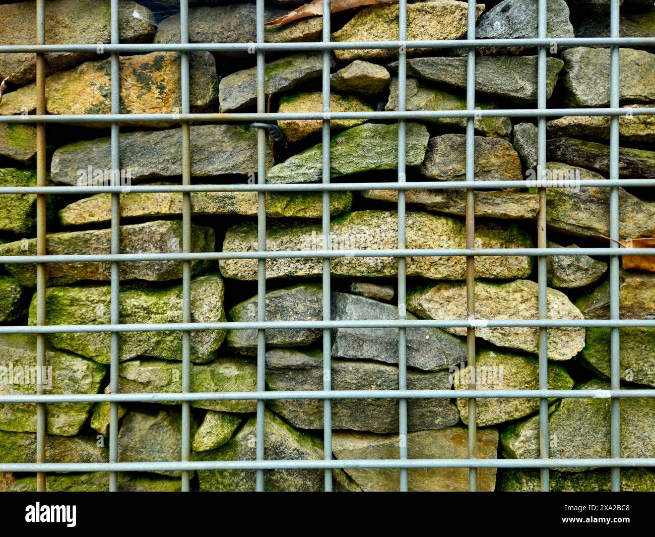 Un primo piano di un muro in pietra dietro una gabbia metallica Foto Stock