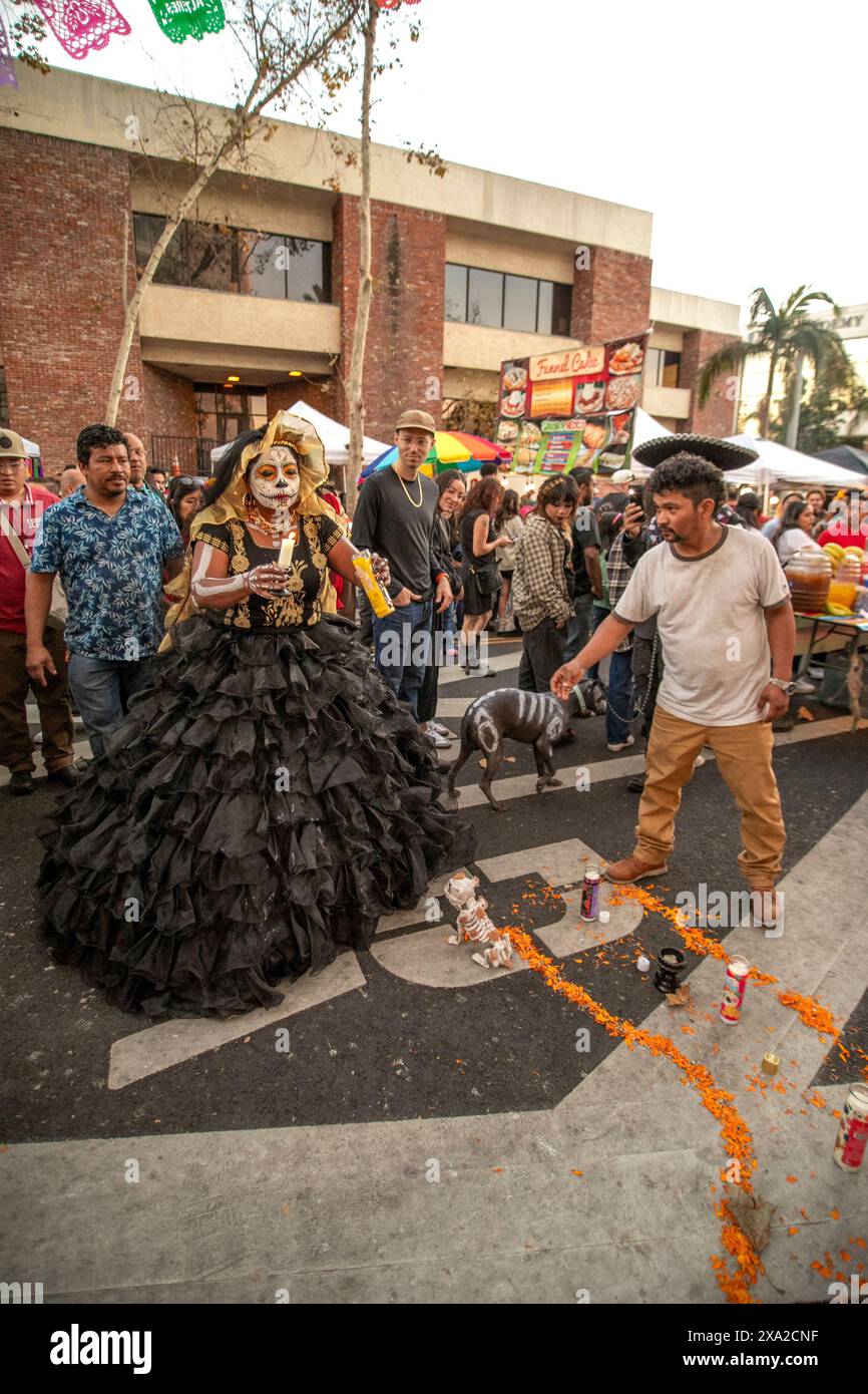 Al festival "Day of the Dead" di Santa Ana, CALIFORNIA, una donna messicana americana vestita con costumi scheletrici e trucco al teschio che indica la morte illumina un certificato Foto Stock