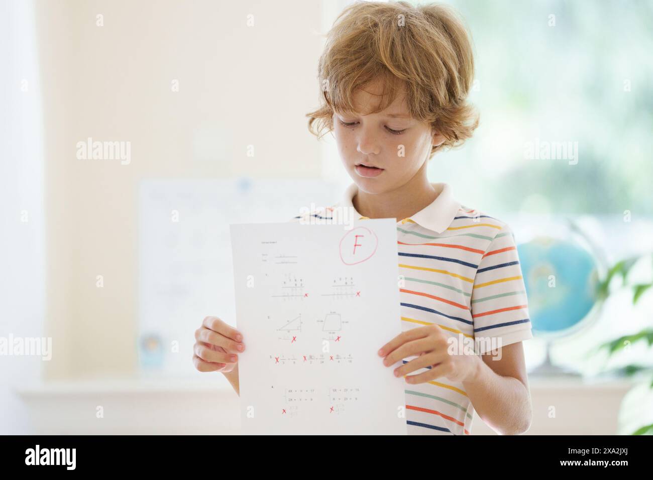 Bambino che tiene il test scolastico con un voto F negativo. Studente turbato dopo l'esame di matematica. Test matematico non riuscito. Ragazzo pianto stressato con carta da lettere fallita Foto Stock