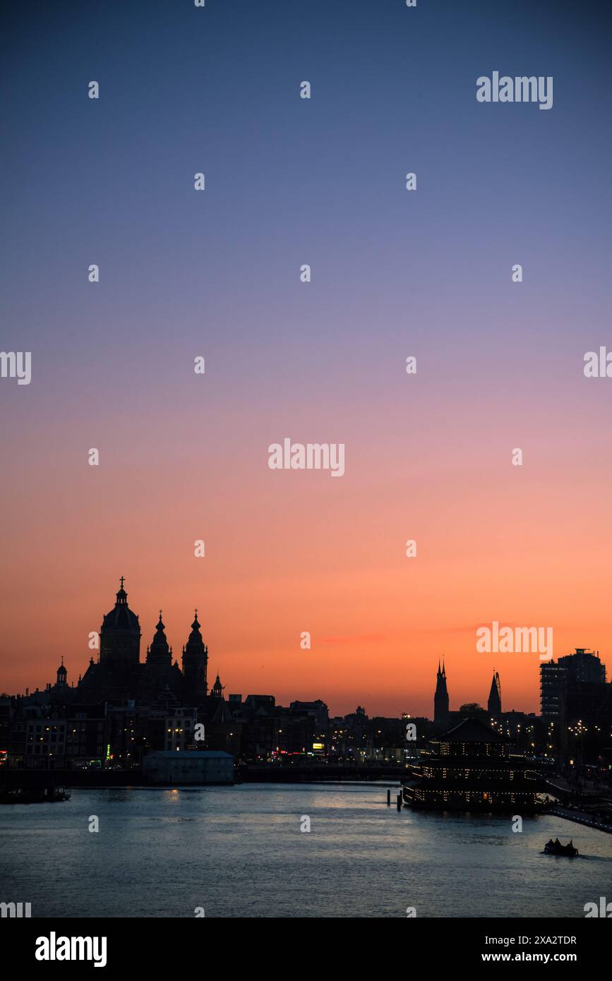 Tramonto sul fiume IJ con la sagoma della basilica di San Nicola in lontananza - Amsterdam, Paesi Bassi Foto Stock