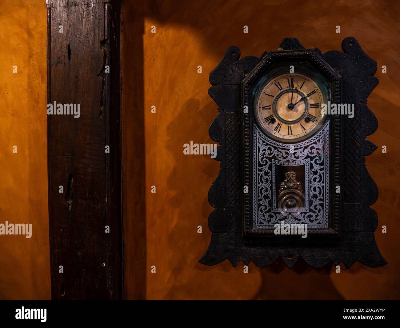 Vecchio orologio a pendolo in legno appeso su un muro rosso Foto Stock