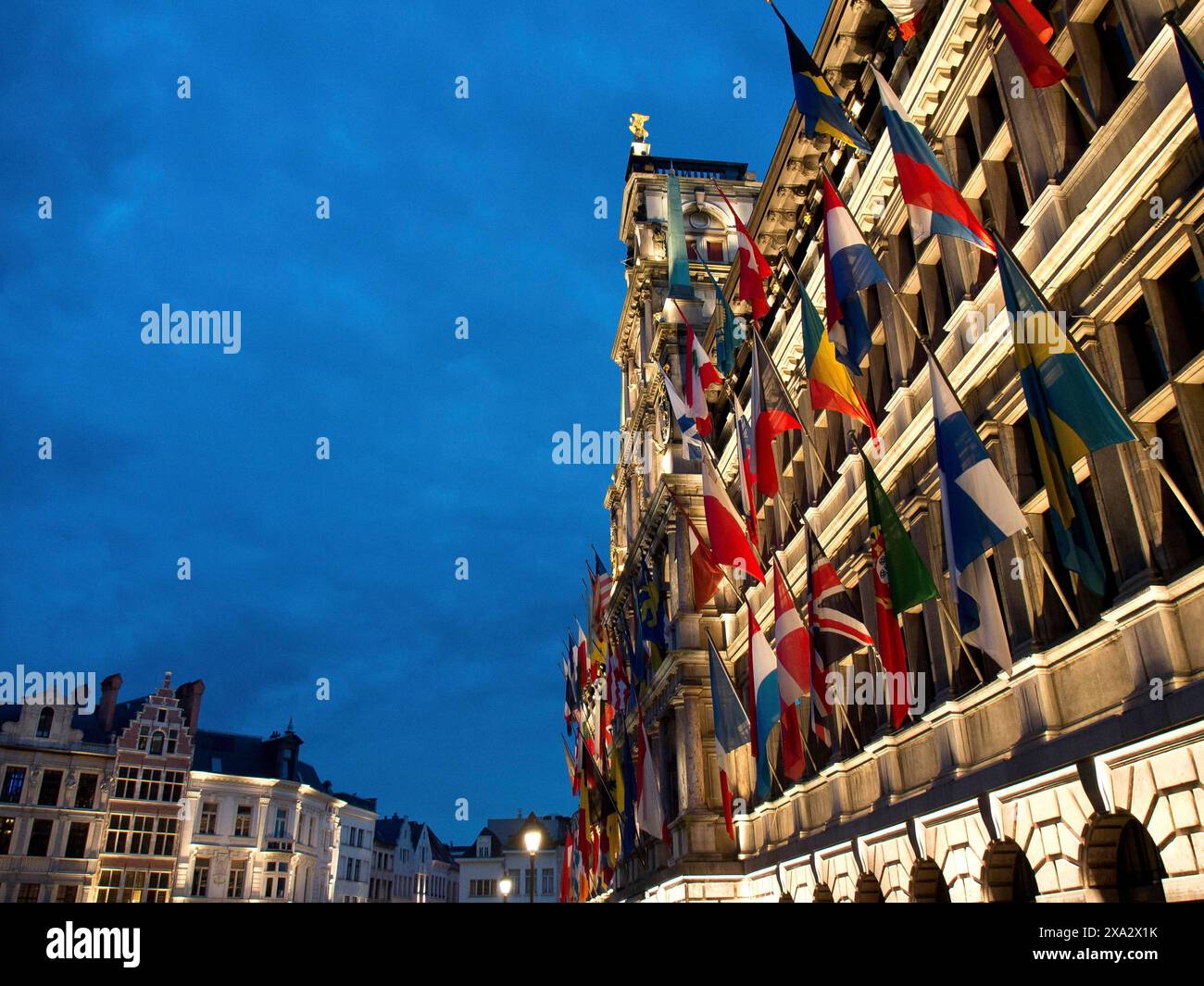 Un edificio illuminato di notte, decorato con numerose bandiere provenienti da diversi paesi, edifici storici sulla piazza del mercato di Anversa Foto Stock