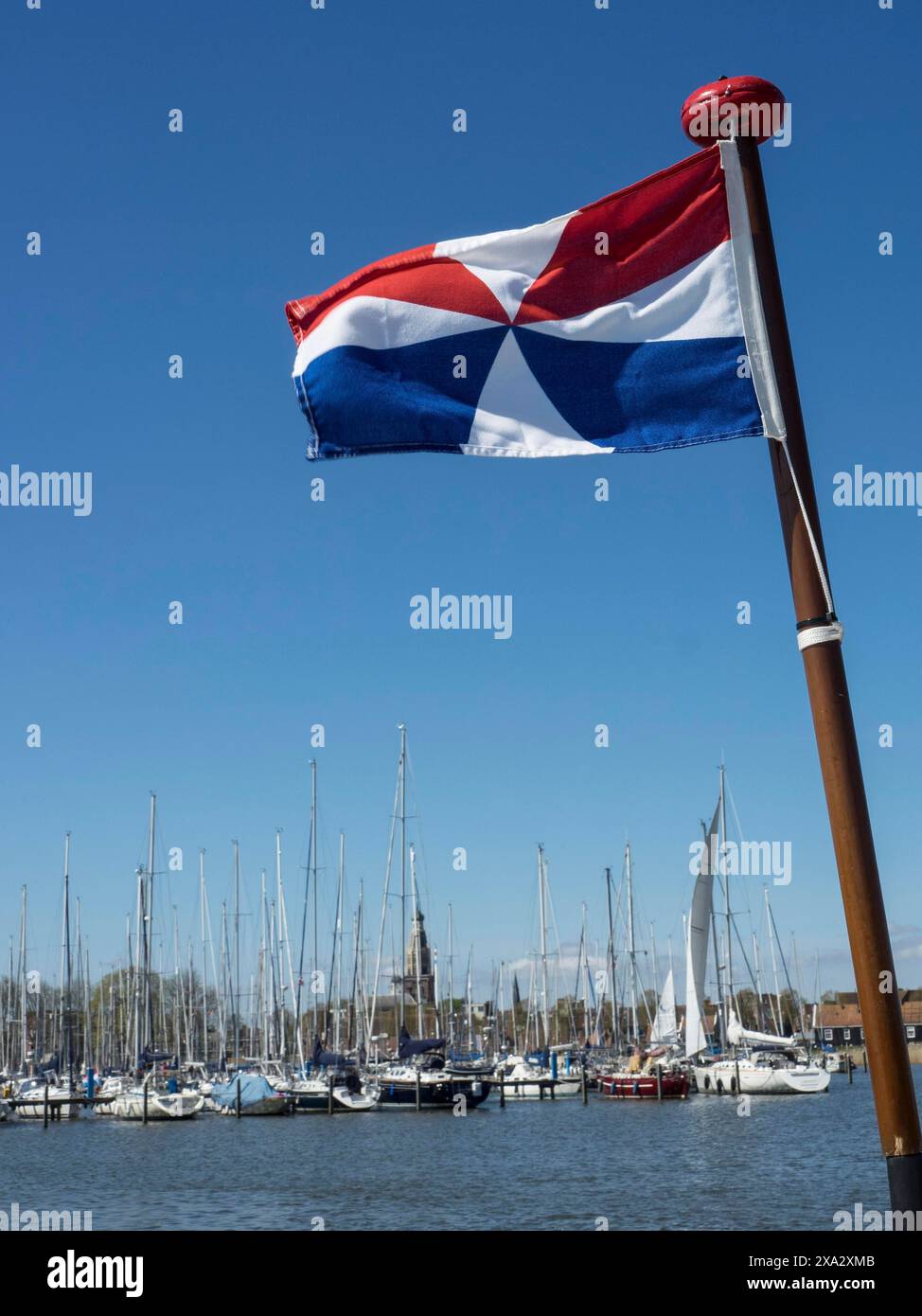 Porto con molte barche a vela e una bandiera rosso-bianco-blu in primo piano sotto un cielo limpido, Enkhuizen, Nirderlande Foto Stock