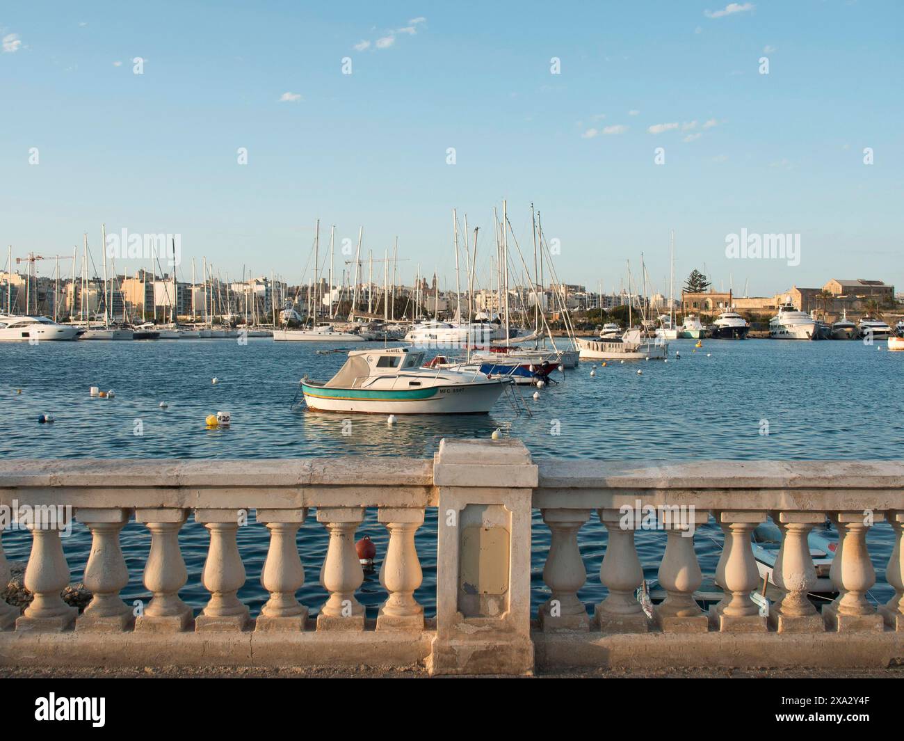 Vista sul porto con numerose barche sul mare calmo e una balaustra in pietra in primo piano, la Valletta, Malta Foto Stock