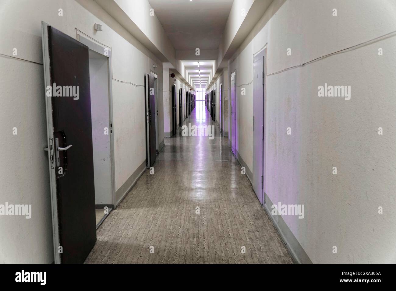 Un lungo corridoio con porte grigie aperte e illuminazione al neon in un vecchio edificio, il Memoriale Berlin-Hohenschoenhausen, ex quartier generale, Stasi remand Foto Stock