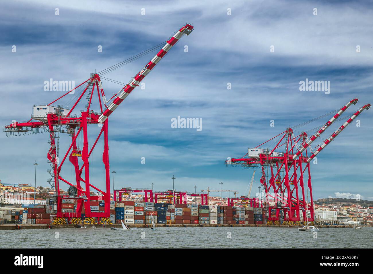 LISBONA, PORTOGALLO - 7 APRILE 2024: Gru rosse e navi container nel porto di Lisbona (Porto de Lisboa), il terzo porto più grande del Portogallo. Foto Stock