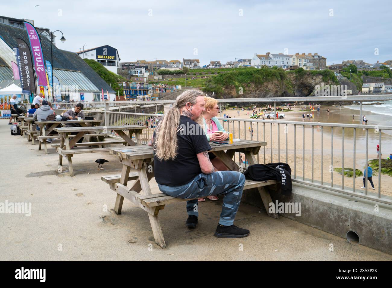 I vacanzieri si rilassano e si siedono ai tavoli da picnic sul lungomare di Towan Beach a Newquay in Cornovaglia nel Regno Unito. Foto Stock