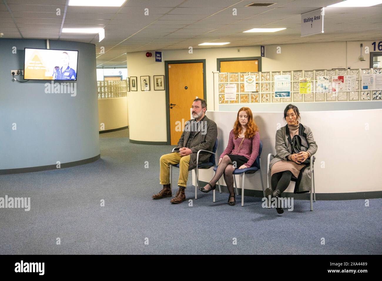 Tre persone sedute in una sala d'attesa di uno studio medico Foto Stock