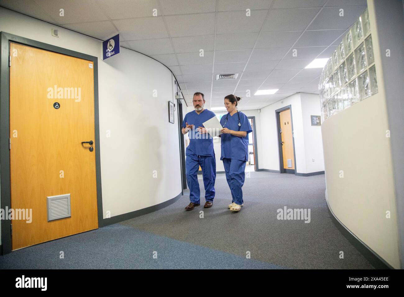 Due operatori sanitari che camminano in un corridoio ospedaliero, studio medico Regno Unito Foto Stock
