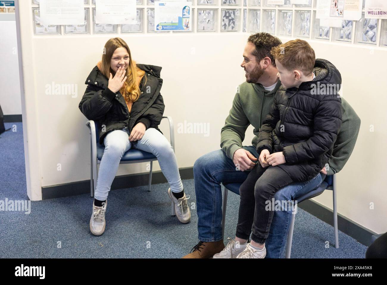 Tre persone sedute in sala d'attesa di uno studio medico, padre, figlio e figlia Foto Stock