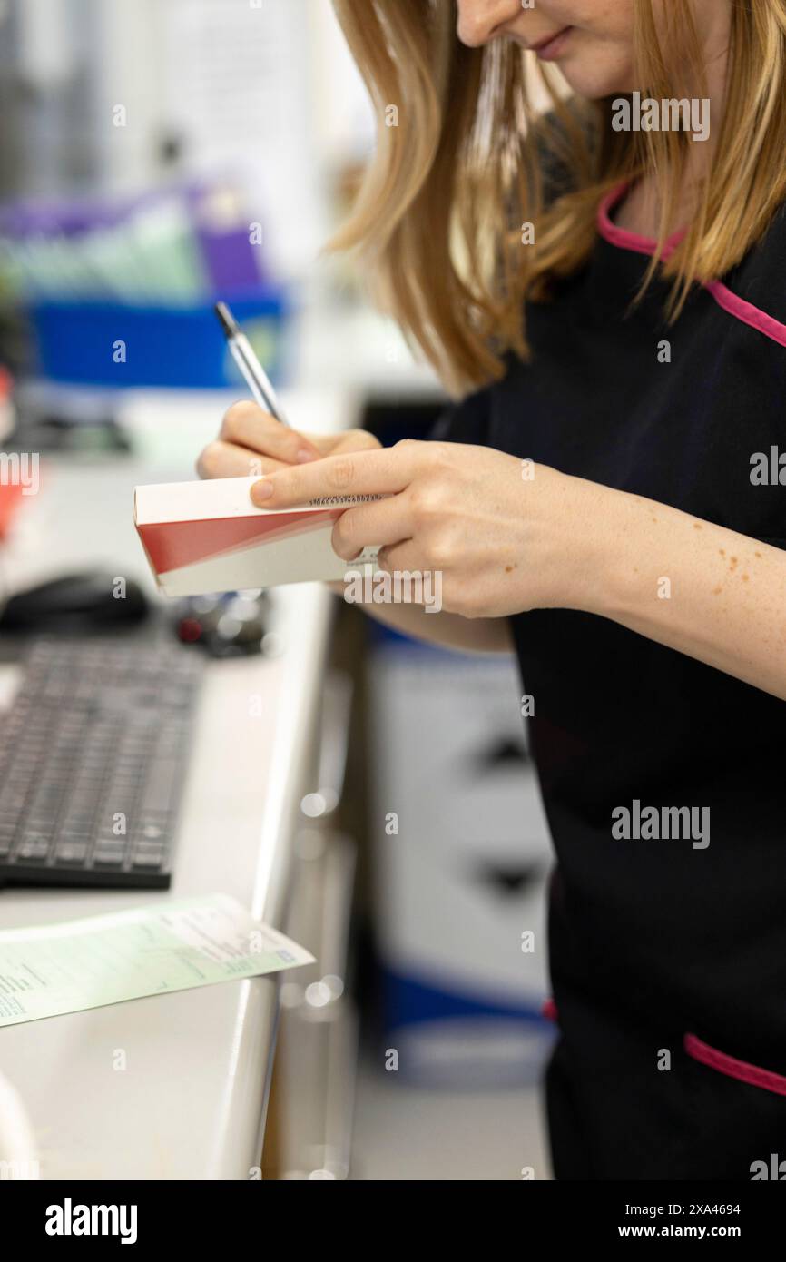 Farmacista che scrive su una scatola di medicinali in una farmacia. Foto Stock