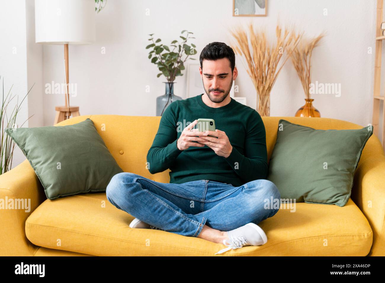 Uomo che usa lo smartphone su un divano giallo Foto Stock