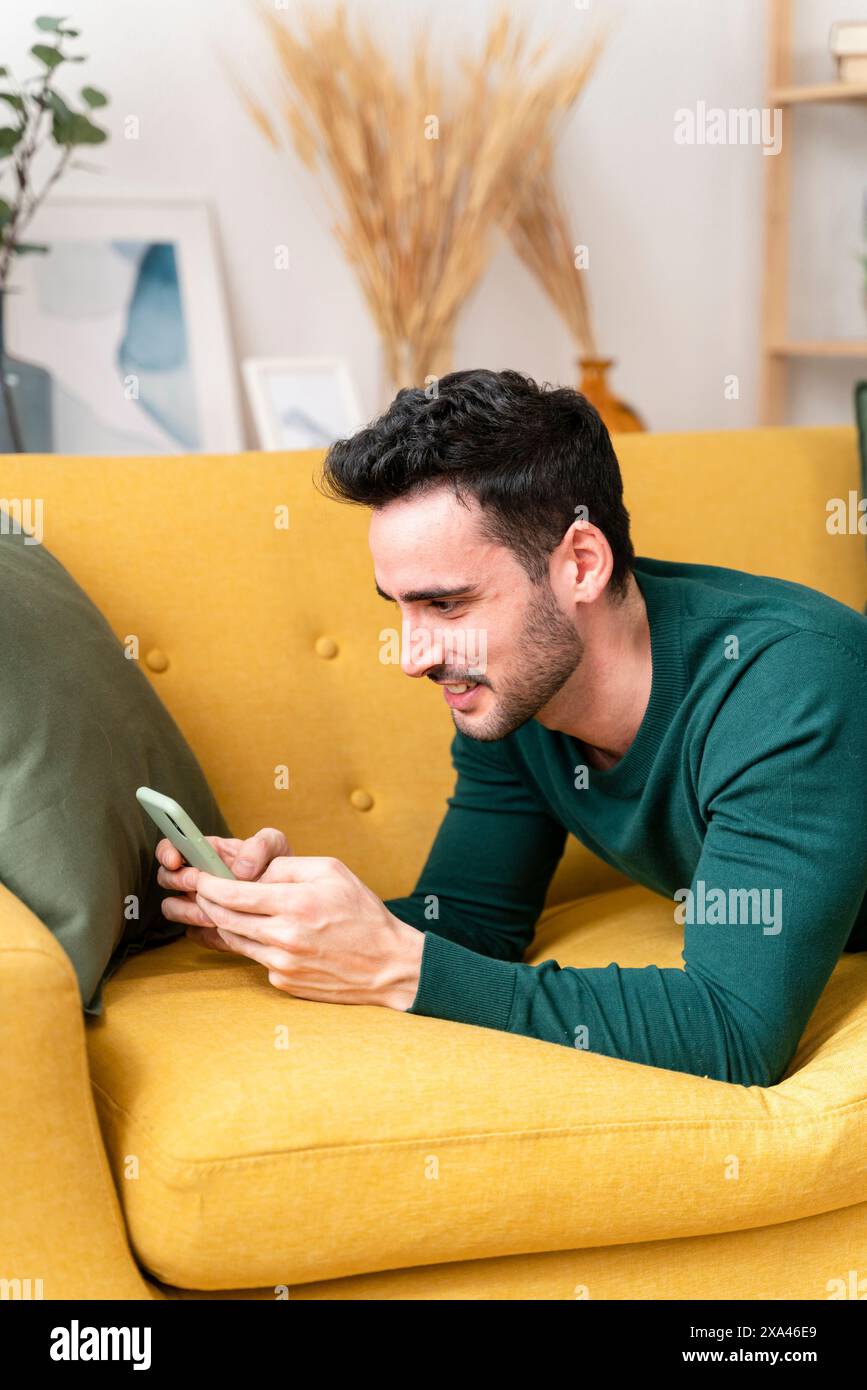 Uomo che usa lo smartphone sul divano giallo Foto Stock
