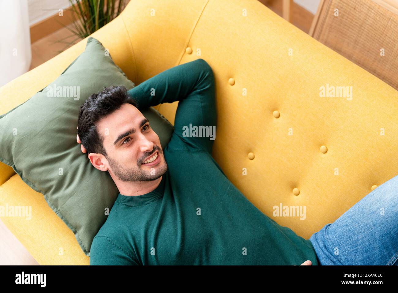 Uomo che si rilassa su un divano giallo con un cuscino verde Foto Stock