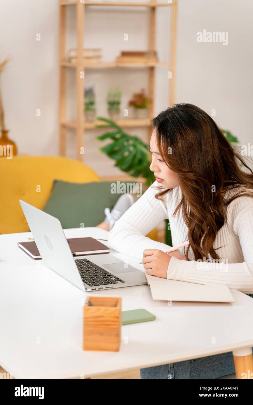 Donna concentrata sul suo notebook in un luminoso ufficio domestico Foto Stock