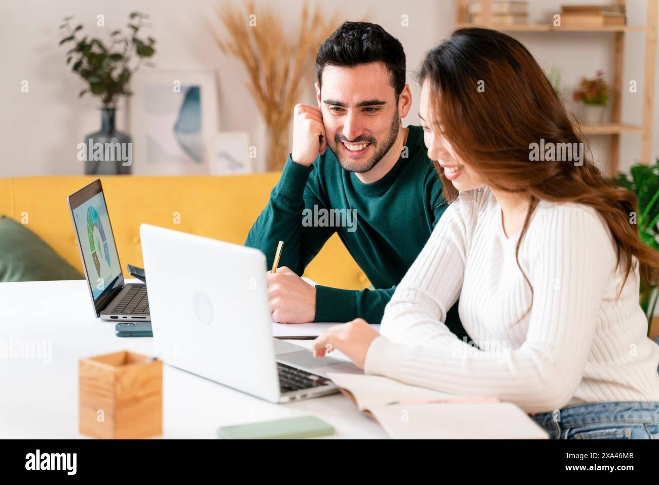 Due persone che sorridono e lavorano con i notebook a un tavolo. Foto Stock