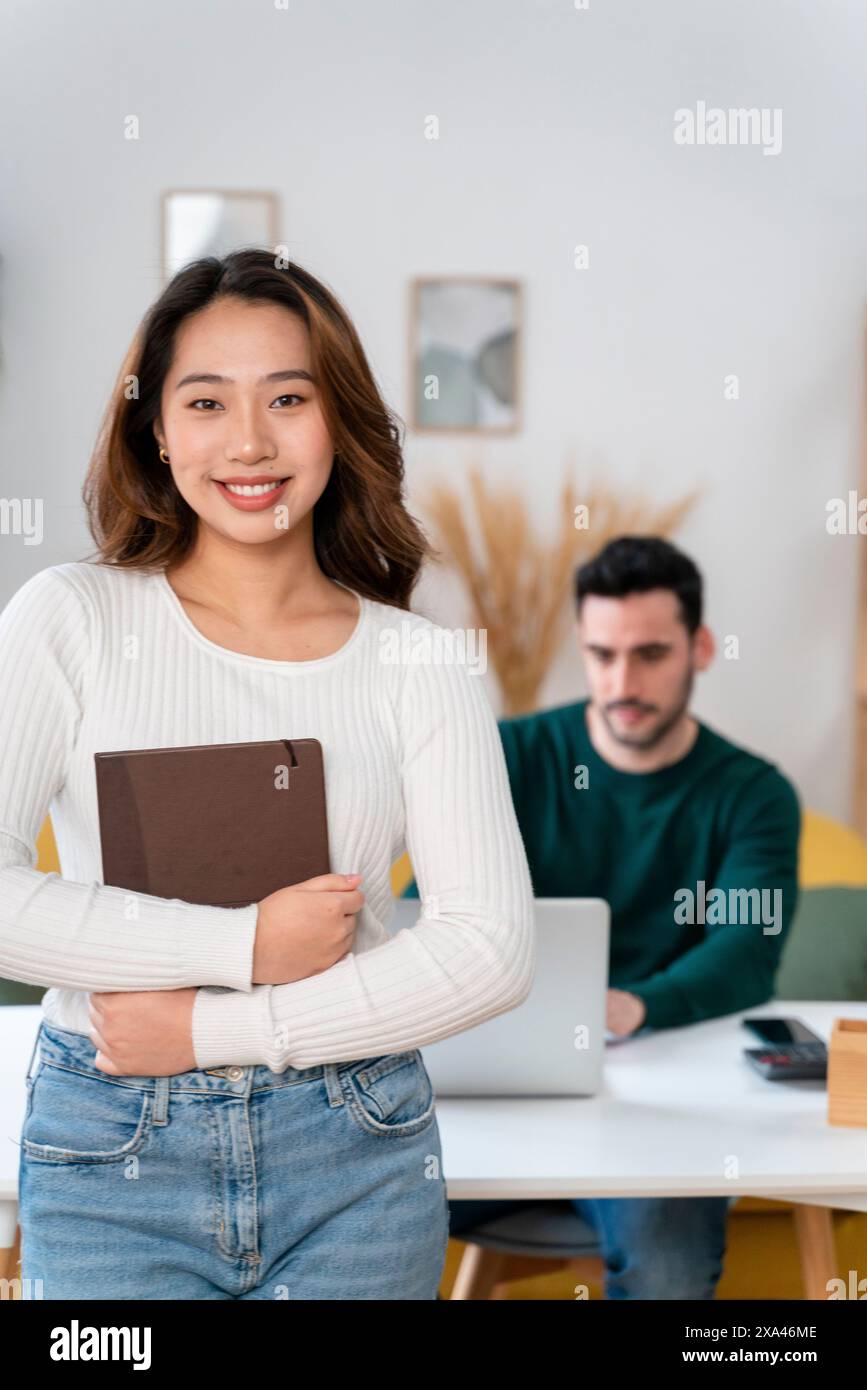 Donna in piedi con un libro davanti a un uomo che lavora su un notebook. Foto Stock