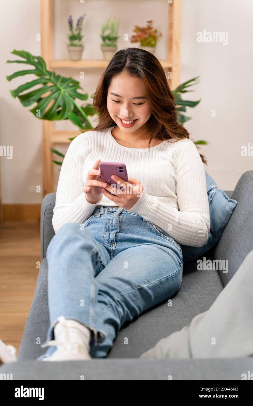 Donna che sorride al telefono mentre è seduta sul divano Foto Stock
