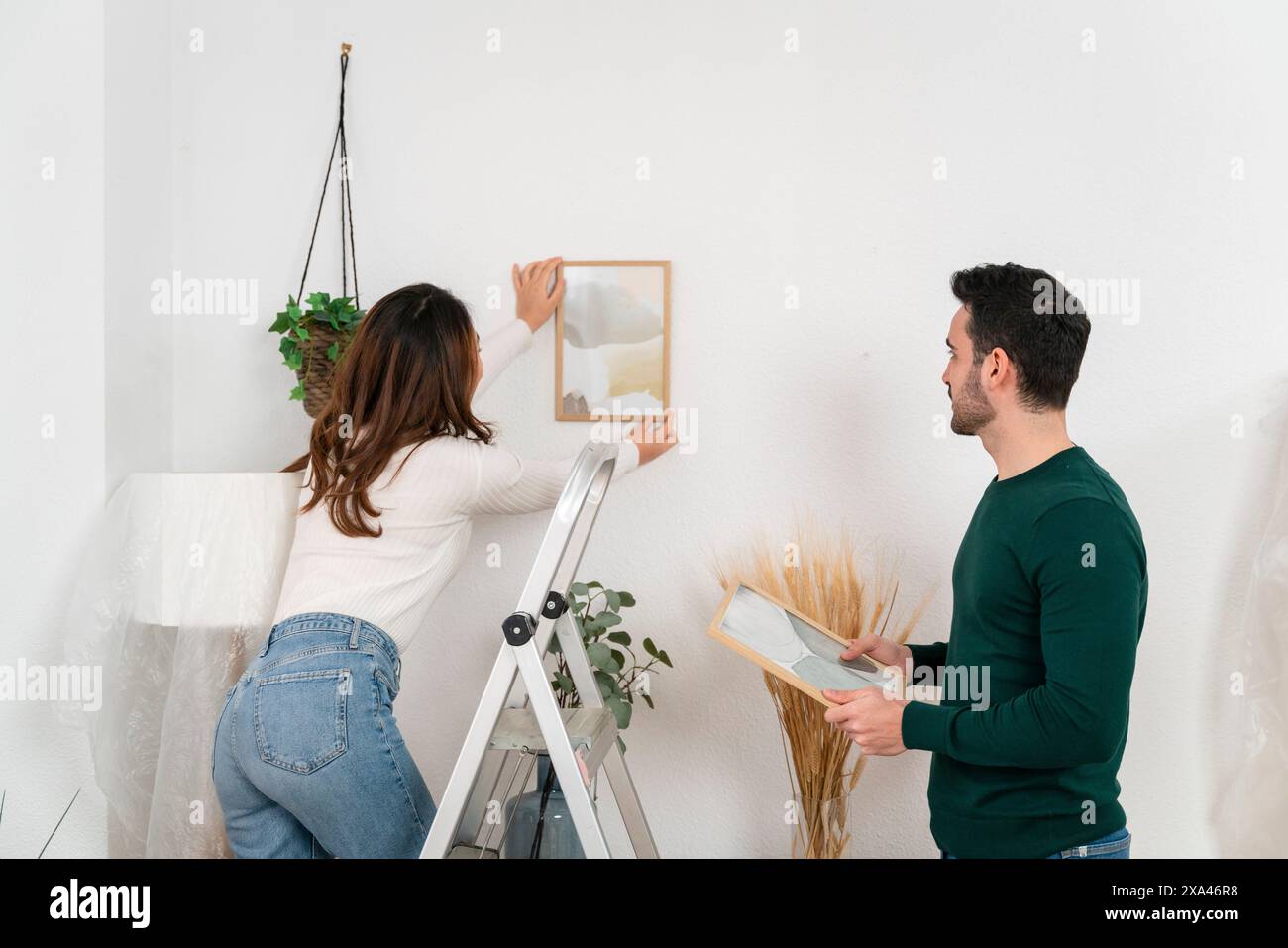 Donna che appende la cornice come osserva l'uomo. Foto Stock